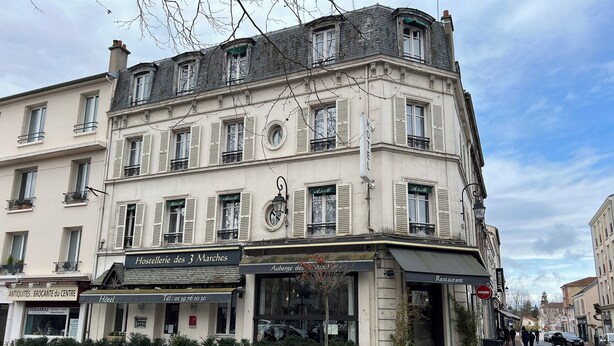 Un hôtel dont l’enseigne, au rez-de-chaussée, porte les inscriptions « Hostellerie des 3 Marches » et « Auberge des Marchés ».