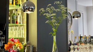 Un coin bar agrémenté d’un vase en verre rempli de fleurs, d’une étagère où sont exposées des bouteilles d’alcool et de luminaires suspendus.