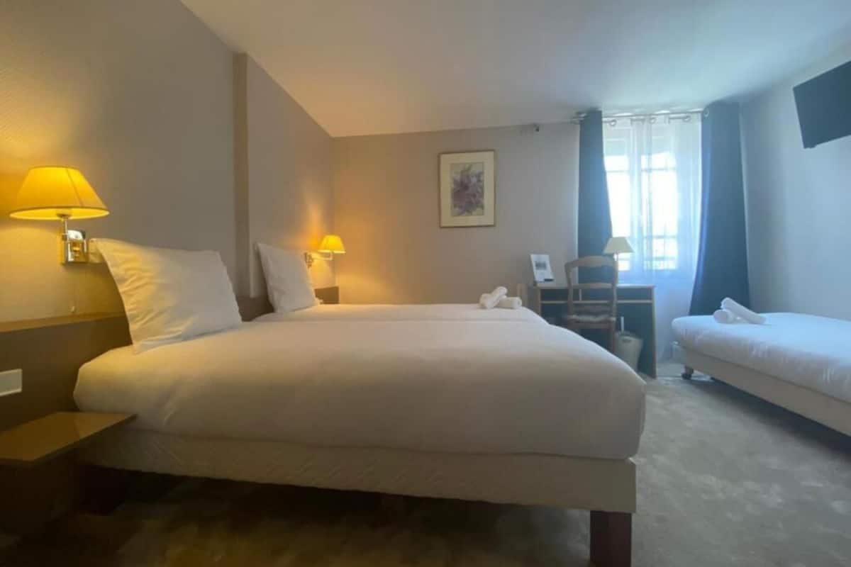 A hotel room with a large bed, two bedside tables with lamps, a chair, a desk, and a small table.