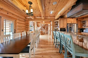 Interior de una cabaña de madera con comedor, cocina y una escalera que sube a una buhardilla.