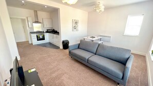 Un apartamento moderno con un sofá gris, una kitchenette, un comedor y una pequeña mesa.