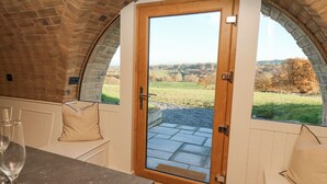 A cozy room with a wooden door leading to a scenic view, a bench, and a table with a glass. - Tan y Wawr- Onnen (Welshpool)
