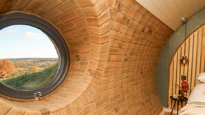 A room with a brick wall, a circular window, a bed, a bedside table, and a wall-mounted light fixture. - Tan y Wawr- Onnen (Welshpool)