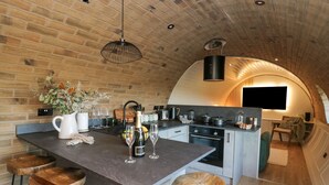 A modern kitchen with a brick wall, a central island with stools, and a built-in oven. - Tan y Wawr- Onnen (Welshpool)