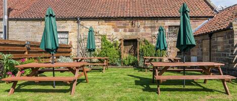 A stone building with a tiled roof, wooden picnic tables, and green umbrellas.