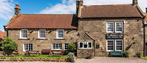 A stone building with a tiled roof, a sign reading "The Witches Post Inn Free House," and outdoor seating.