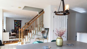 Una cocina moderna con una isla grande, una escalera de madera y un comedor con sillas color turquesa.