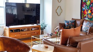 Una sala de estar con un televisor de pantalla plana grande, un sofá de cuero marrón y un tapiz colorido en la pared.