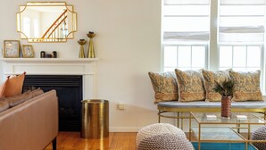 Una sala de estar con sofá, reposapiés, mesa de centro, chimenea y una ventana con persianas.