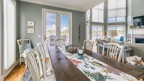 A dining room with a long table, chairs, and a view of the outdoors. - Golf and Ocean Views, 6 seat golf cart included (Fripp Island)