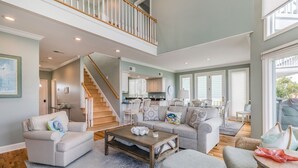 A spacious living area with a high ceiling, a staircase, and a kitchen in the background. - Golf and Ocean Views, 6 seat golf cart included (Fripp Island)