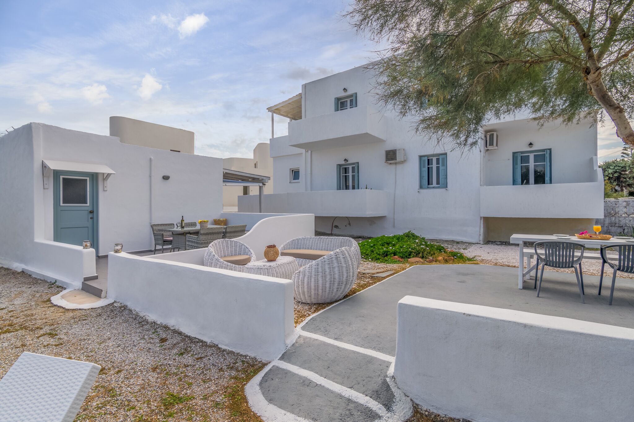 A modern white building with outdoor seating and a tree.