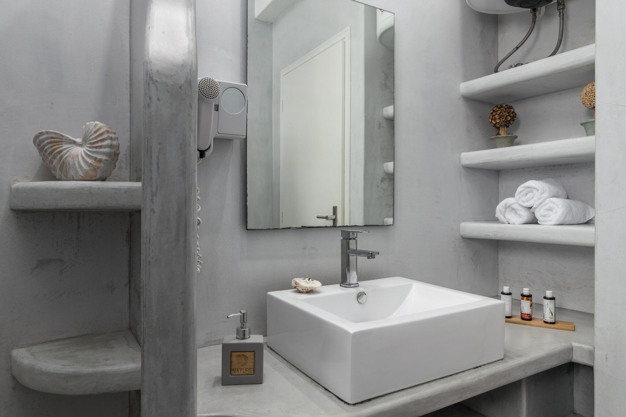 A modern bathroom with a white sink, a large mirror, and built-in shelves with toiletries.