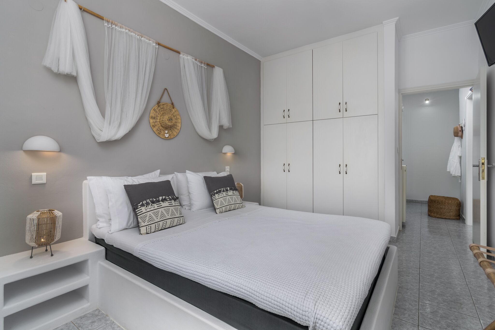 Una camera da letto moderna con un letto grande, tende bianche, una lampada da comodino e un armadio.