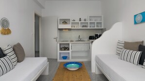 A compact room with a kitchenette, two beds, and a dining table with a bowl. - Venia's Guesthouse (Milos)
