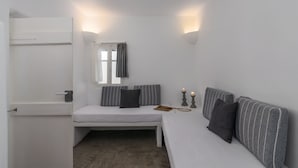 A small, white room with a bed, a bench, and a window with curtains. - Venia's Guesthouse (Milos)