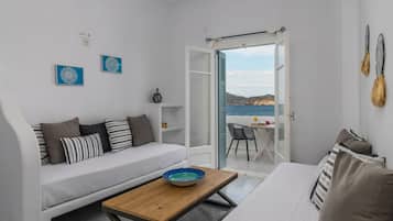 Habitación compacta con sofá, una mesita y vista al mar a través de una puerta abierta.