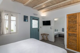 Quarto com cama, janela com cortinas, porta, televisão e uma pequena mesa.