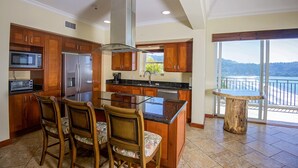 Cocina moderna con armarios de madera, electrodomésticos de acero inoxidable, una isla de vidrio y vista a la playa.