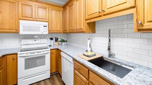 A kitchen with wooden cabinets, a white microwave, a stove, a dishwasher, and a granite countertop. - Near downtown Cary & RDU. Easy access to Raleigh, Durham and local venues. (Cary)