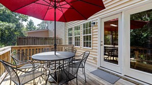 A wooden deck with a round table and chairs, a red umbrella, and a white door leading to an outdoor area. - Near downtown Cary & RDU. Easy access to Raleigh, Durham and local venues. (Cary)
