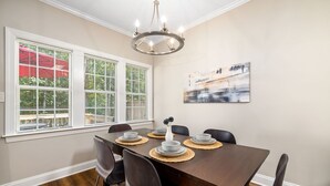 A dining area with a wooden table set for six, six chairs, a chandelier, and a painting on the wall. - Near downtown Cary & RDU. Easy access to Raleigh, Durham and local venues. (Cary)