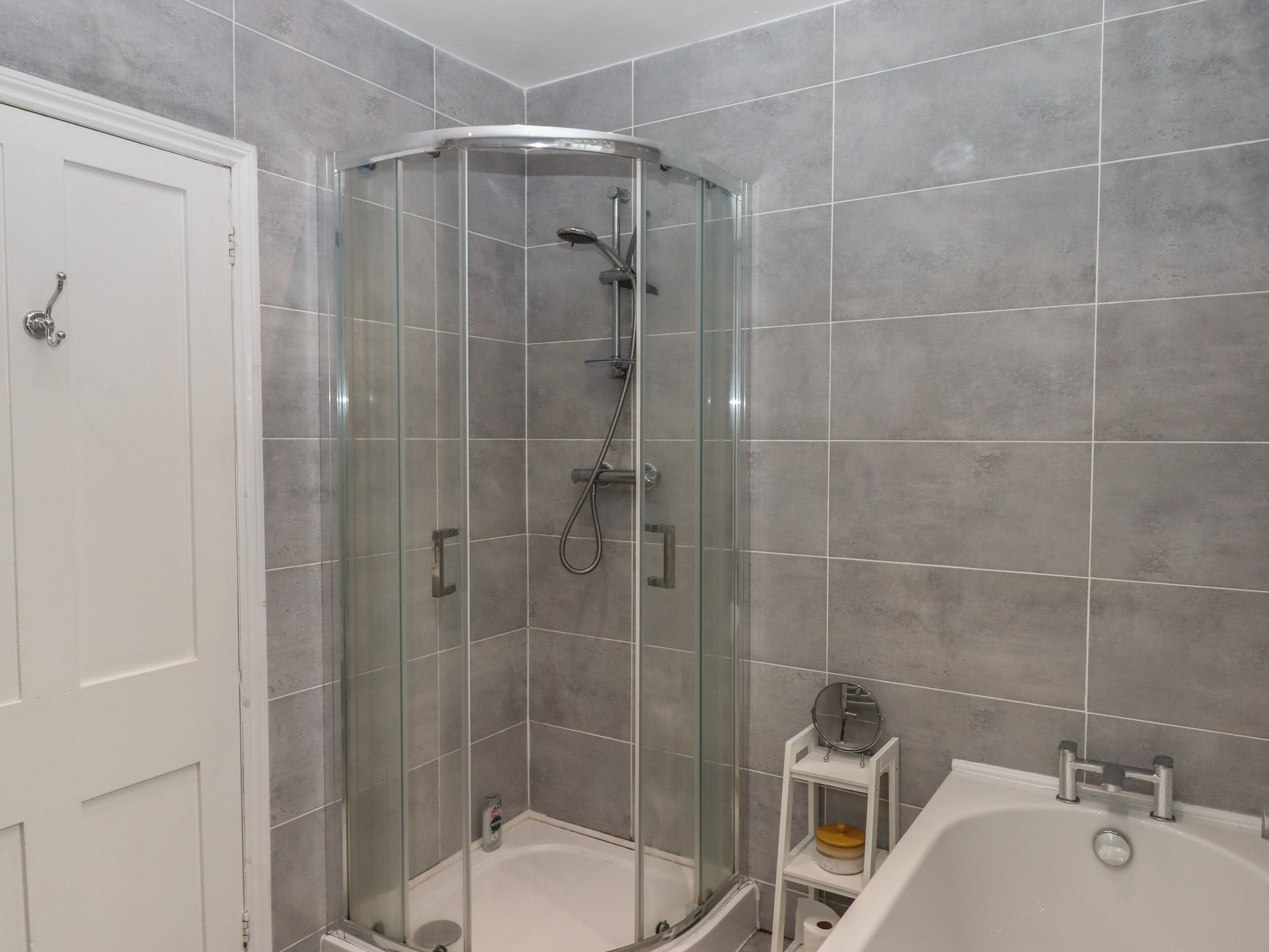 Un baño con ducha acristalada, una bañera blanca y un pequeño estante con artículos de aseo.