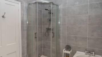 Un baño con ducha acristalada, una bañera blanca y un pequeño estante con artículos de aseo.