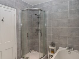 Un baño con ducha acristalada, una bañera blanca y un pequeño estante con artículos de aseo.