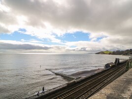 Vías de tren costeras con vista al mar y colinas al fondo.