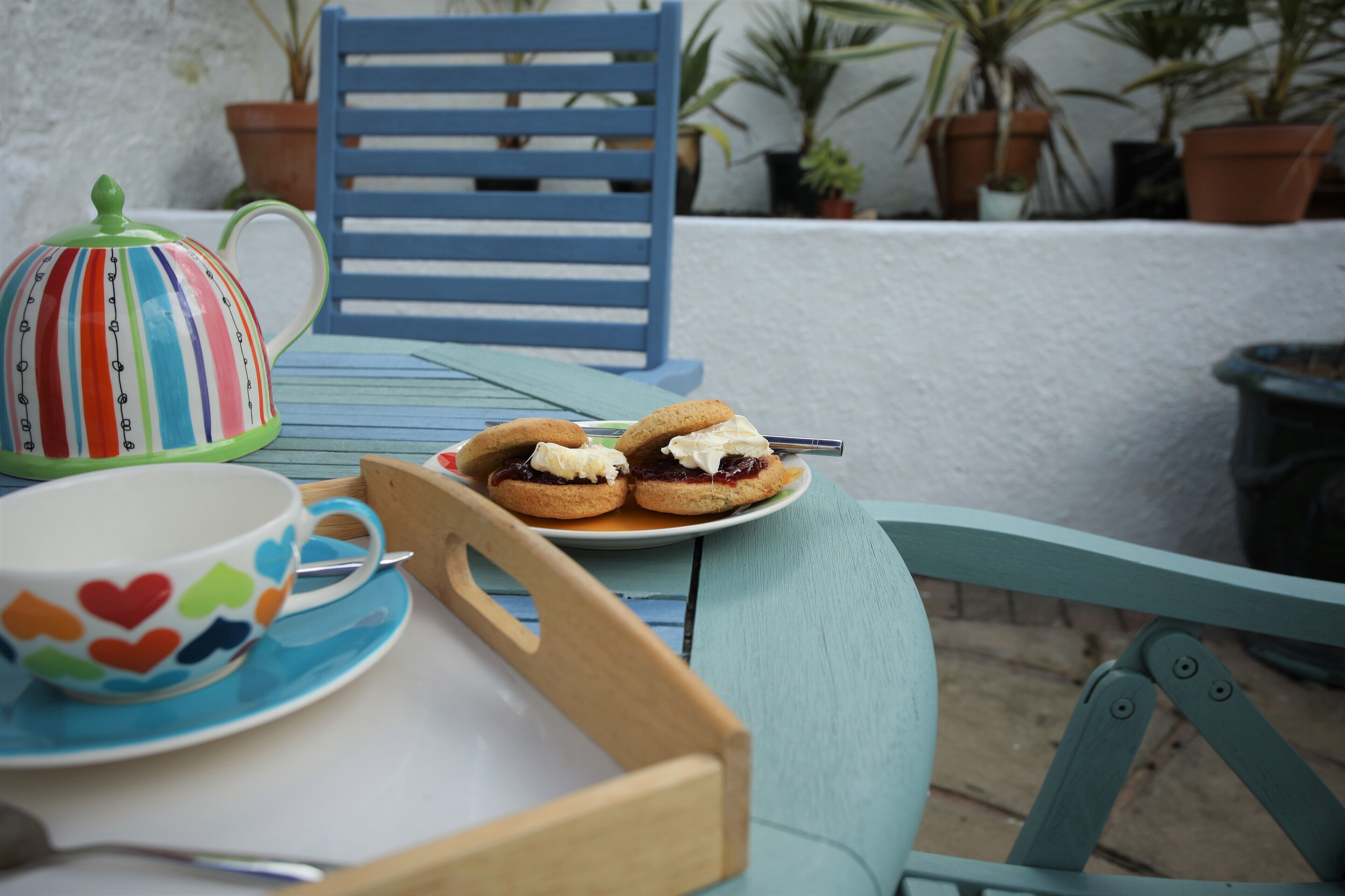 Una mesa con una bandeja, una tetera, una taza y dos scones con mermelada y crema.