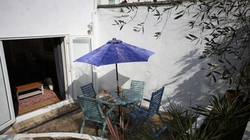Un pequeño patio al aire libre con una mesa, sillas, un paraguas azul y plantas en macetas.