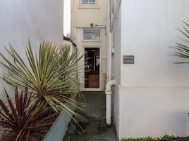 Un estrecho callejón con un edificio blanco, una puerta que dice "Mimosa Cottage" y una planta de hojas largas.