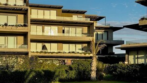 Un immeuble moderne à plusieurs étages, doté de balcons et de grandes fenêtres, entouré d’une pelouse bien entretenue et d’un chemin de gravier.