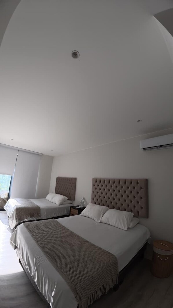 Una habitación de hotel moderna con dos camas, un ventanal grande y un equipo de aire acondicionado.