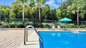 A swimming pool with a metal ladder, surrounded by palm trees and a fence.