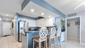 A modern kitchen with white cabinets, a stainless steel refrigerator, and a bar area with two stools.