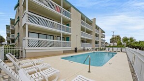 A modern hotel with a pool area, multiple balconies, and white sun loungers.
