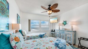 Ein Schlafzimmer mit Bett, Deckenventilator, Fenster, Fernseher und Kommode.