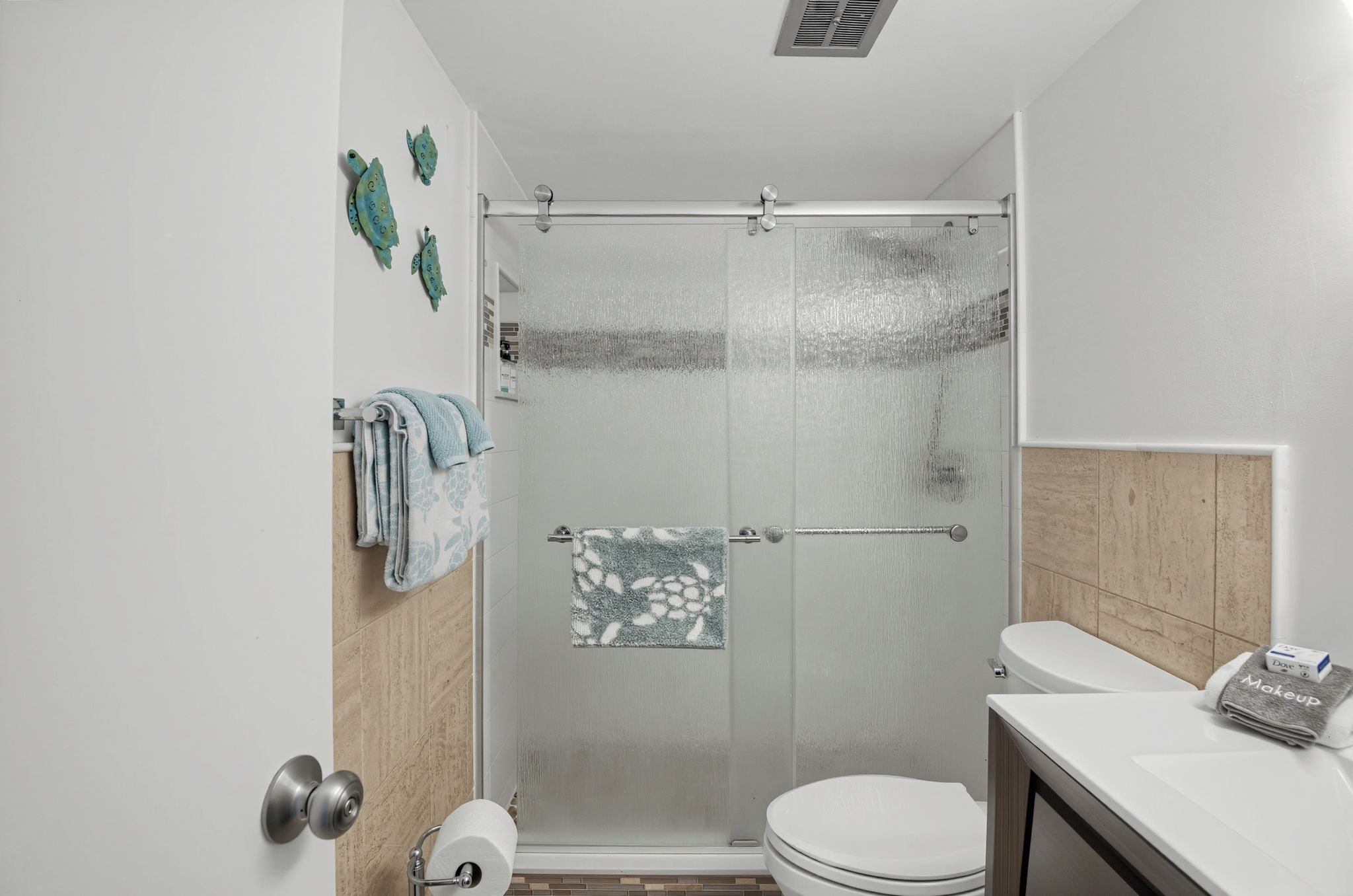 A bathroom with a glass shower enclosure, a toilet, a sink, and decorative wall art.