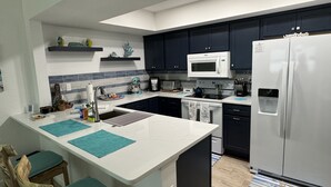 Eine moderne Küche mit dunklen Schränken, einem weißen Kühlschrank, einer Mikrowelle und einem Spülbecken.