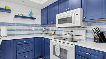 A kitchen with blue cabinets, a white microwave, a kettle, and a knife block.