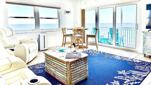 Ein Zimmer mit Meerblick, einem Deckenventilator, einem Tisch mit Stühlen und einem Stapel Bücher.