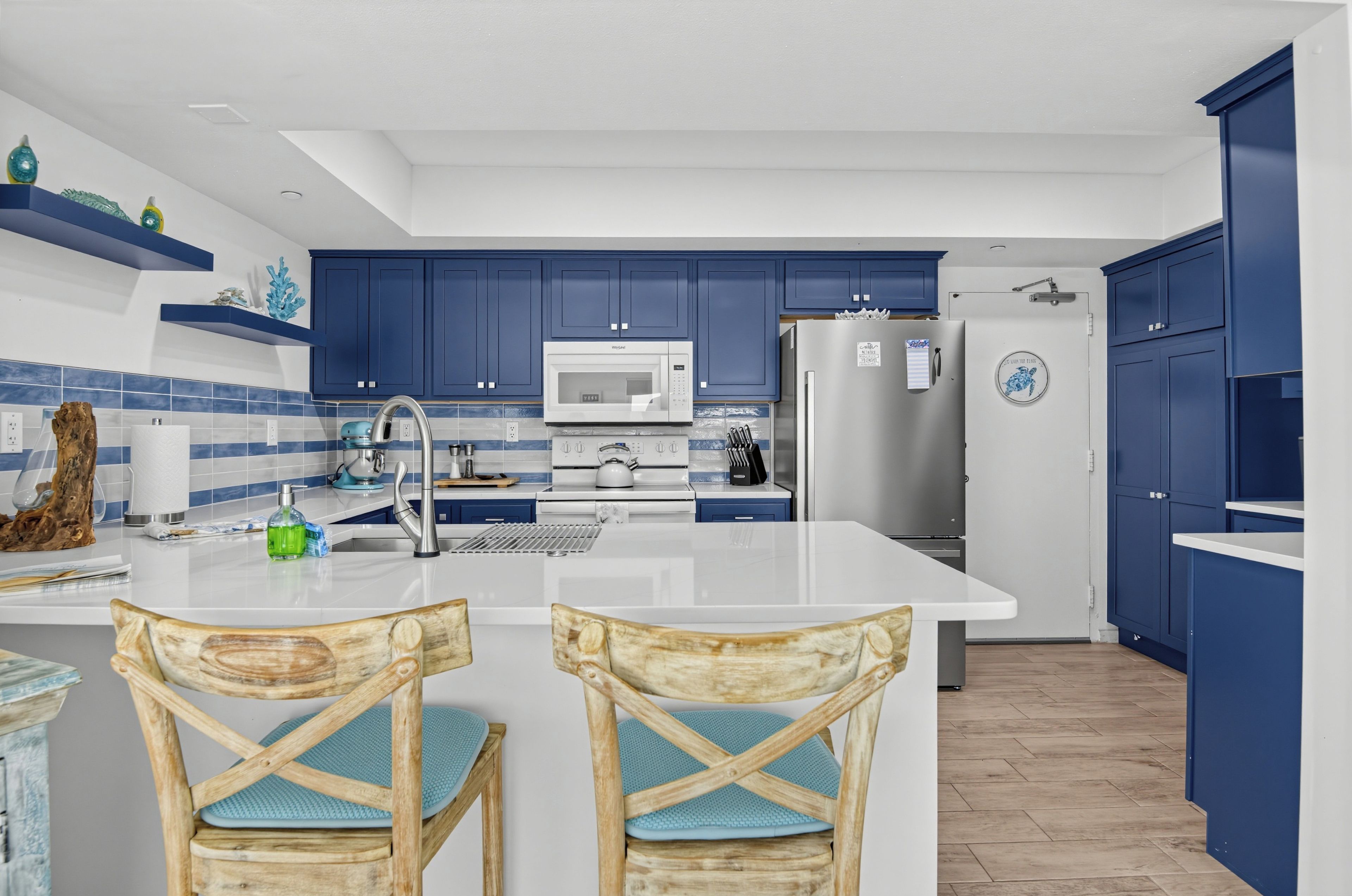 A modern kitchen with blue cabinets, a white island, and a stainless steel refrigerator.