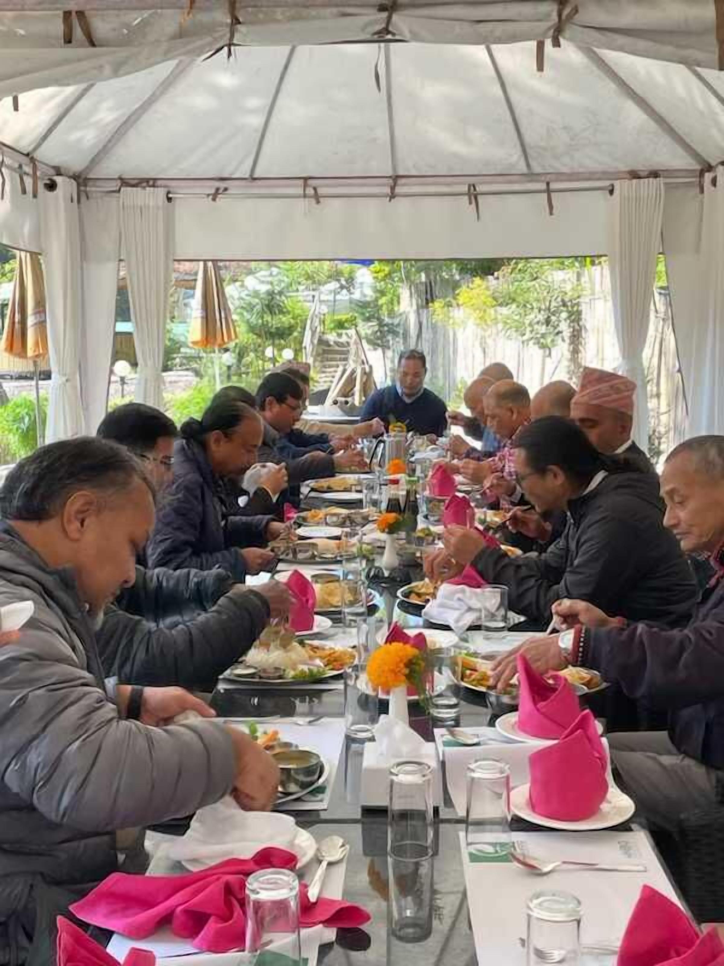 A group of people dining at a table under a tent, with various dishes and drinks.