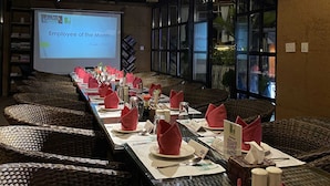 Une salle de conférence avec une longue table préparée pour une réunion, un écran de projection affichant une présentation et une vue sur l’extérieur grâce à de grandes fenêtres.