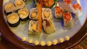 Un plateau de sushis comprenant différents types de sushis, notamment des nigiris et des makis, disposés sur une assiette en céramique.