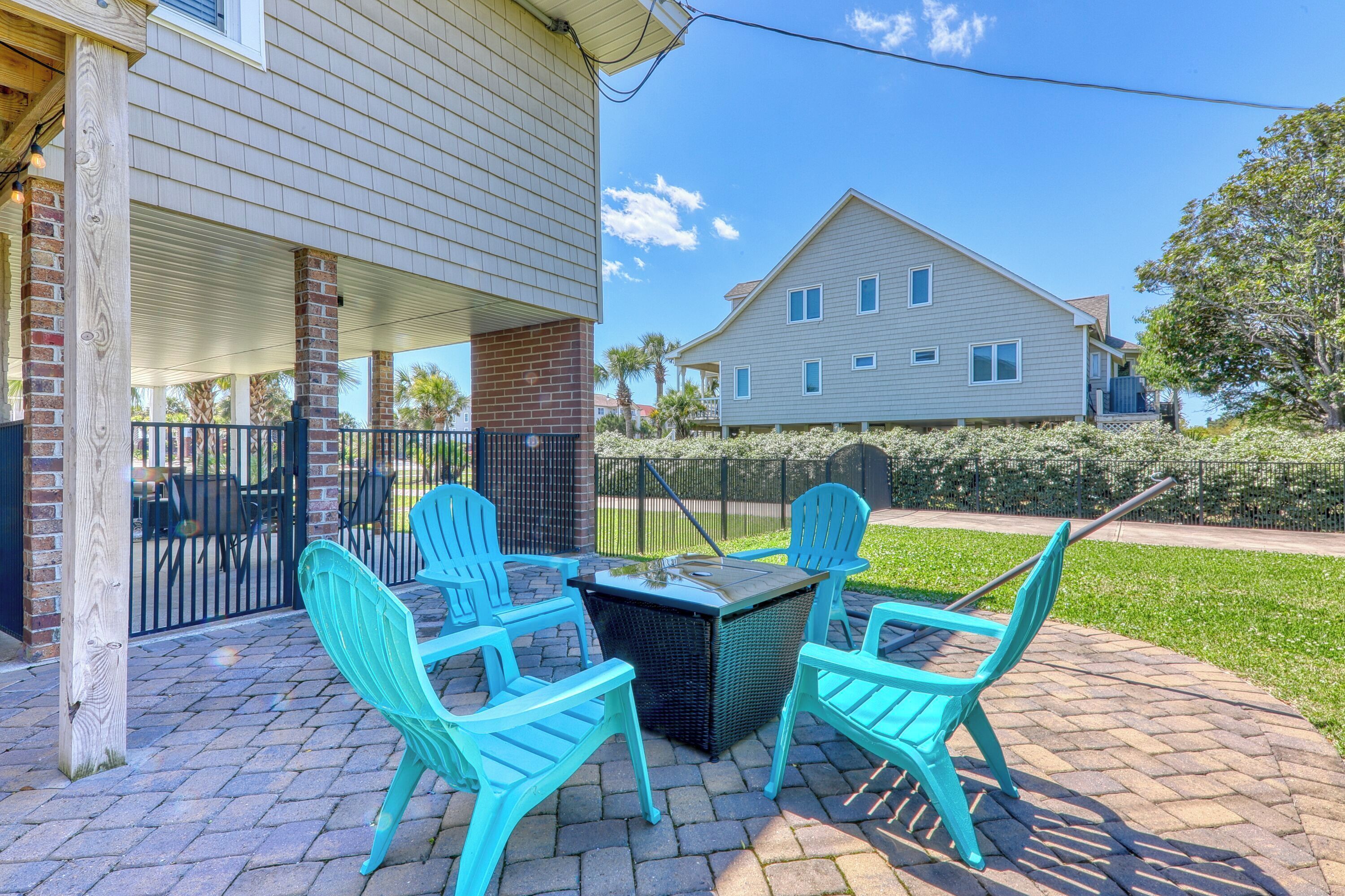 A patio with four turquoise chairs and a table, a brick wall, and a house in the background.
