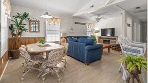 Ein geräumiges Wohnzimmer mit Essbereich, einem blauen Sofa, einem Fernseher und einem Deckenventilator.