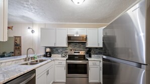 A modern kitchen with white cabinets, stainless steel appliances, and a marble countertop.